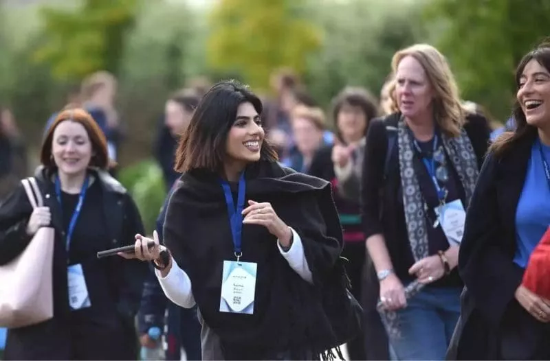 Group of people outdoors wearing conference badges, smiling and walking together.