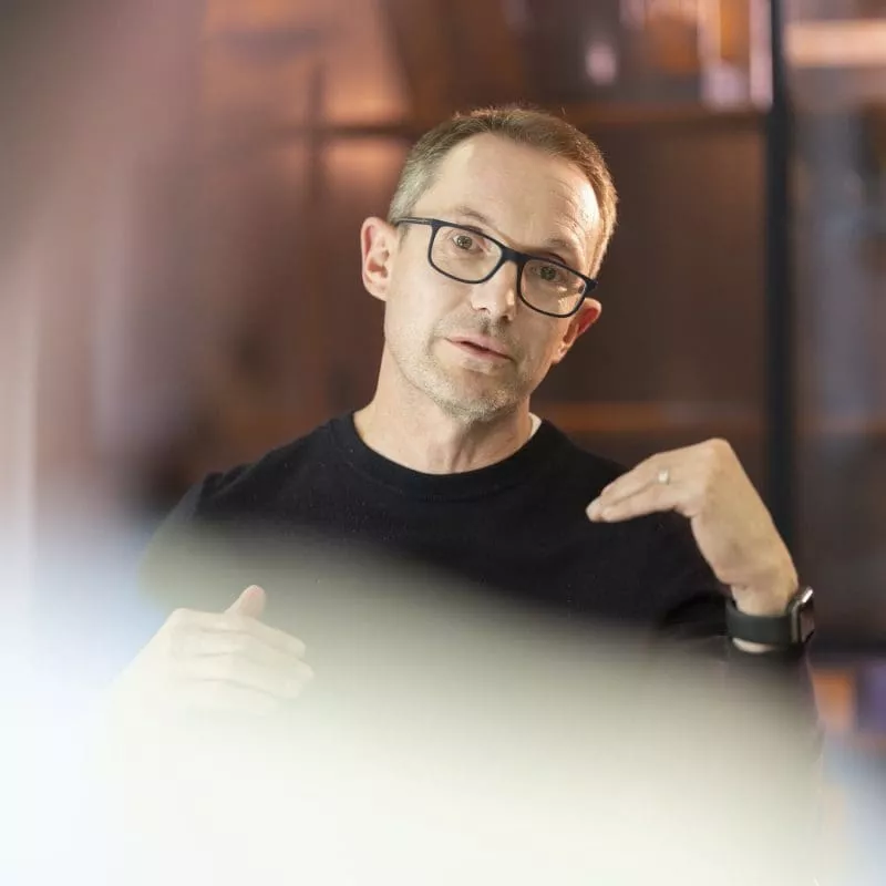 Person wearing glasses speaking and gesturing during a discussion.