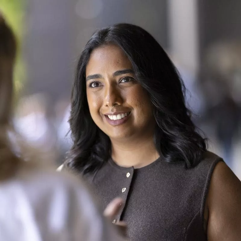 Person smiling and listening during a conversation, wearing a sleeveless dark top.