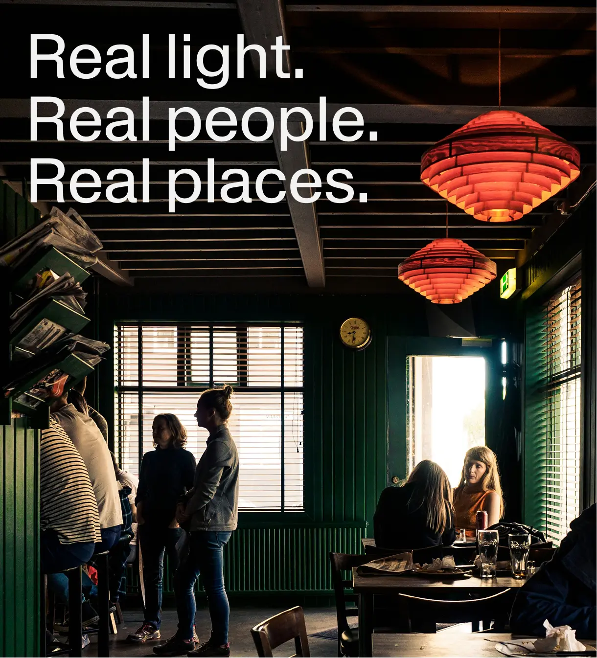 A documentary-style photograph of two workers at an HS Orka geothermal facility in Iceland. One person in workwear and a hard hat is adjusting or inspecting industrial equipment with visible pipes and control elements, while another stands nearby observing. The background shows rugged volcanic terrain and infrastructure elements under natural light, conveying the scale and environment of geothermal energy operations. The image highlights people at work in an outdoor industrial-landscape setting, reflecting HS Orka’s focus on energy, engineering, and place. (From HS Orka brand photography on Brandpie.)